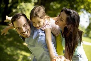 Familia joven feliz con linda hijita divirtiéndose en el parque en un día soleado foto