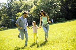 Familia joven feliz con linda hijita corriendo en el parque en un día soleado foto