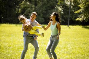 Familia joven feliz con linda hijita corriendo en el parque en un día soleado foto