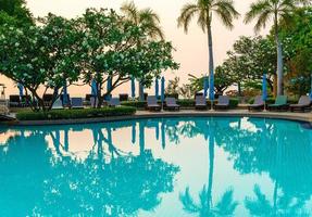 Beach chairs or pool beds with umbrellas around swimming pool at sunset time photo