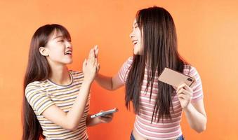 Two beautiful young Asian girls using mobile phones on orange background photo