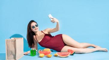 Asian woman in red bikini lying and using phone to take selfie photo