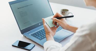 Asian businesswoman writing down information from laptop screen photo