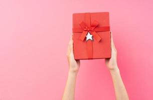 Hands holding red gift box on pink background