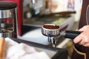 A female worker presses the finely ground coffee beans against a tamper photo