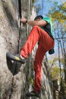 A bearded man aged with a bag of magnesia and rock shoes is trainered on a not high rock in the woods. Training of climbers in natural conditions photo