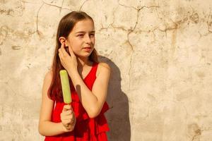 A girl 10 or 11 years old on a hot sultry day in a red dress. Summer teenager girl with ice cream. photo