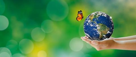 Hand holding earth with butterfly over green blur background photo