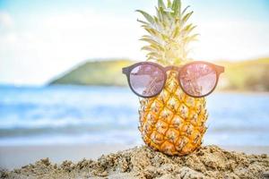 El vidrio del sol está en la piña en la playa con vistas al mar, concepto de vacaciones de verano foto