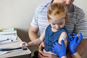 una niña con su padre en el consultorio del médico en la clínica está siendo vacunada contra el coronavirus. el concepto de vacunación, inmunización, prevención contra el covid-19. foto