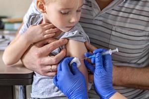 una niña con su padre en el consultorio del médico de la clínica está siendo vacunada contra el coronavirus. el concepto de vacunación, inmunización, prevención contra covid-19. foto