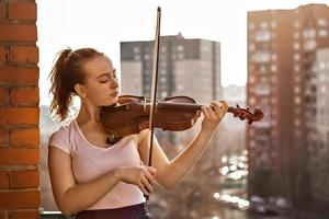 una niña, un músico, toca el violín en el balcón de su apartamento