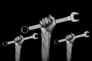 foto en blanco y negro. tres llaves en las manos de las mujeres. manos sostiene unas llaves sobre un fondo gris. llave combinada. llave grande de cromo vanadio en la mano. trabajo de mujeres. Día laboral
