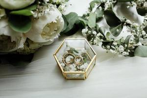 Wedding details. two classic gold wedding rings in a glass box and a bouquet of white flowers and greenery photo