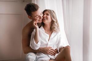 loving couple having fun together at home, playful wife biting smiling husband ear, piggyback, man and woman playing childish in bed, enjoying funny intimate moments photo