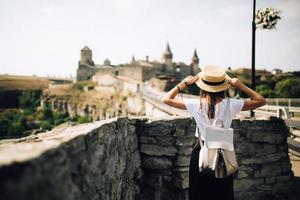 Woman tourist with backpack and hat enjoys traveling to historical places in Ukraine, castle in Kamianets-Podilskyi. Rear view. Selective focus photo