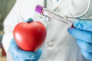 Positive blood infection sample in test tube for covid-19 coronavirus in lab. Scientist holding red heart to encourage patient in hospital. photo