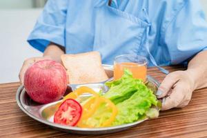 Asian senior or elderly old lady woman patient eating breakfast vegetable healthy food with hope and happy while sitting and hungry on bed in hospital. photo