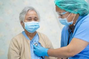 médico que usa estetoscopio para verificar que el paciente asiático mayor o anciano usa una mascarilla en el hospital para proteger la infección por el coronavirus covid-19. foto