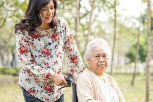 Paciente asiático mayor o anciano con cuidado, ayuda y apoyo en silla de ruedas en el parque en vacaciones, concepto médico fuerte y saludable. foto