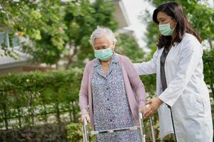 El médico ayuda a una anciana asiática mayor o anciana a caminar con un andador y con una mascarilla para proteger la infección de seguridad y matar el nuevo virus coronavirus covid-19. foto