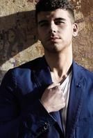 Handsome young man with blue eyes posing near a wall photo