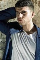 Handsome young man with blue eyes posing near a wall photo