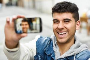 Young man selfie in urban background with a smartphone