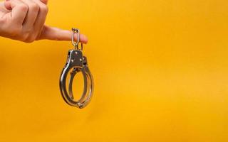 female hand holding handcuff with copy space on yellow background, illegal arrest photo