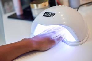 Manicured nails in UV lamp in beauty salon. photo