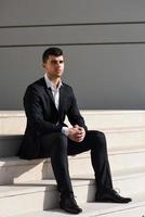 joven empresario cerca de un edificio de oficinas con traje negro foto