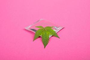 condón y hoja de marihuana en un primer plano de fondo rosa foto