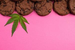 chocolate chip cookie with marijuana leaf on pink background copy space, sweets with cannabis photo