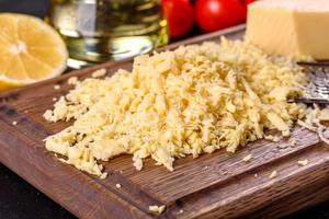 Fresh hard cheese grated on a large grater on a wooden cutting board photo