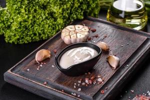 Garlic sauce in a ceramic black sauce with greenery on a wooden cutting board photo