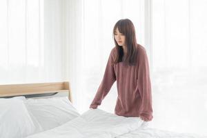 Mujer asiática haciendo la cama en la habitación con sábana blanca limpia foto