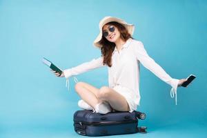 Young Asian woman holding plane ticket and phone sitting on suitcase photo