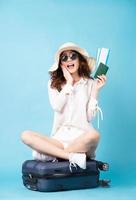 Young Asian woman holding plane ticket and phone sitting on suitcase photo