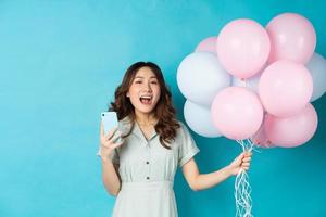Young Asian woman holding balloons and using phone