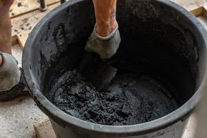 La mano del hombre sostiene una paleta y mezcla de cemento en un balde. foto