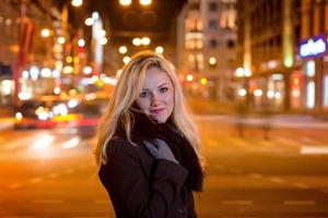 mujer hermosa, rubia en las luces del coche en la ciudad de noche. foto