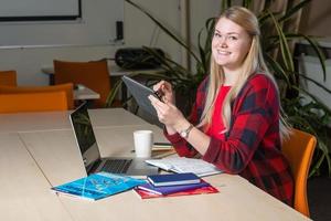 Smiling blonde woman sitting at a laptop drinking tea and working. photo