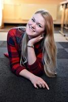 A smiling blonde woman in a red checkered shirt lying on the floor. photo