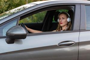 una mujer joven y hermosa con cabello largo y auriculares se sienta al volante del auto. foto