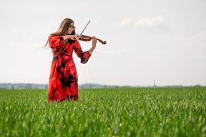 Mujer joven en vestido rojo tocando el violín en la pradera verde - imagen foto