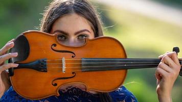 Portrait of a positive young woman. Part of the face is covered by the neck of the violin - image