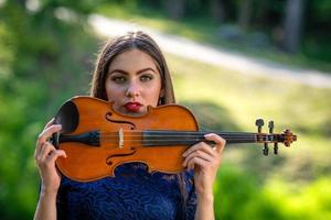 Portrait of a positive young woman. Part of the face is covered by the neck of the violin - image