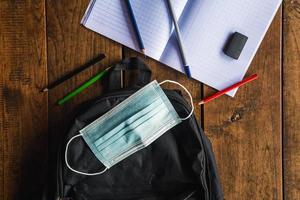 máscara protectora y mochila escolar, útiles escolares en el escritorio de la escuela, medidas de coronavirus y concepto de regreso a la escuela foto