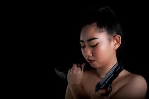 Asia woman one hand holding a gun and karambit knife at the black background