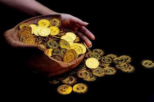 Moneda de oro en la mano en lotes apilando monedas de oro en el frasco del tesoro roto fondo blanco foto
